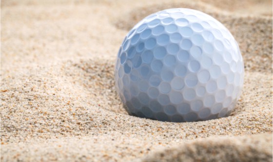 A golf ball plugged deep in sand trap.