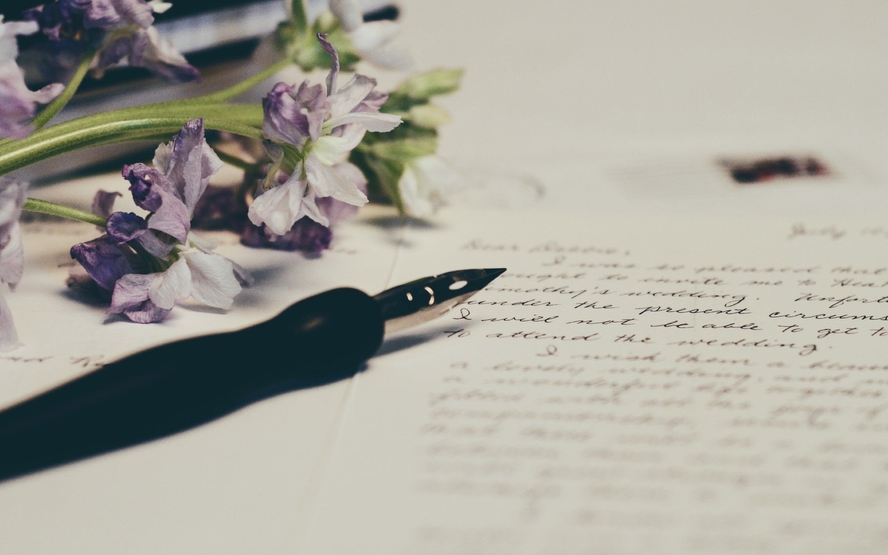 A pen lying on a white piece of paper that has some writing on it, next to purple flowers