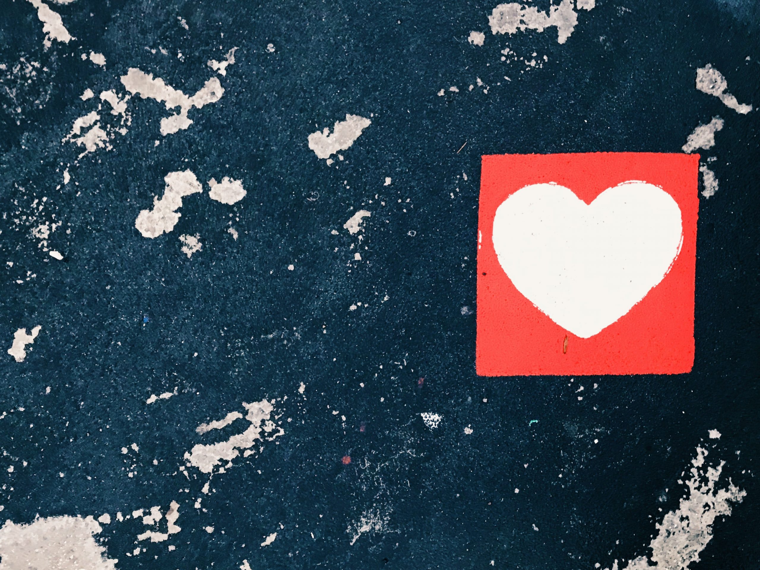 A white heart on a read square background, against a blue and white surface