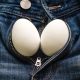Two white chicken eggs on jeans as a symbol of male testicle