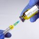 Hands in blue gloves are typing a yellow vaccine in a syringe