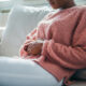 Woman in painful expression holding hands against belly suffering menstrual period pain, lying sad on home bed, having tummy cramp in female health concept