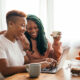 Happy gay couple having breakfast working on laptop